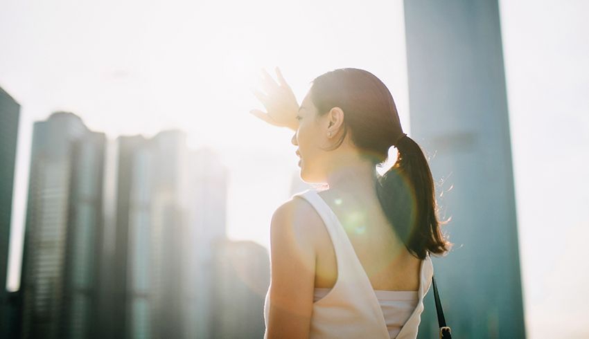 A woman shielding her eyes from the sun shining between buildings in the city